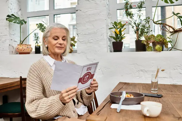 A mature woman smiles while reading a menu in a charming cafe filled with greenery. — Stock Photo
