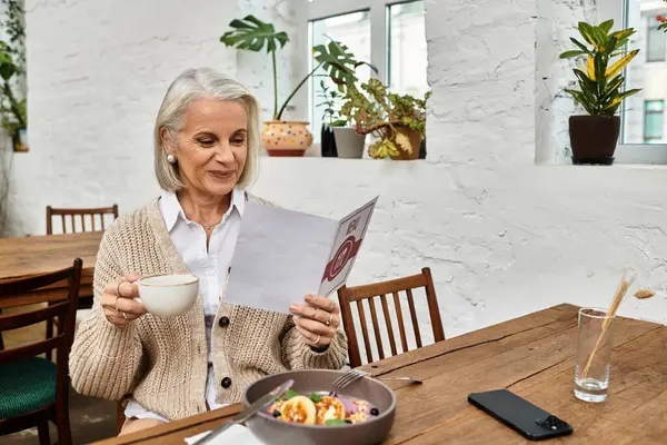 With a warm smile, a graceful woman sips tea while deciding on her brunch order in a charming cafe. — Stock Photo