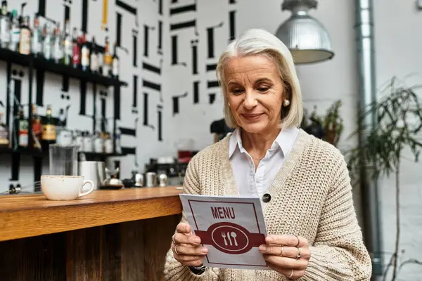 The beautiful mature woman examines a menu while seated in a warm, inviting cafe atmosphere. — Stock Photo
