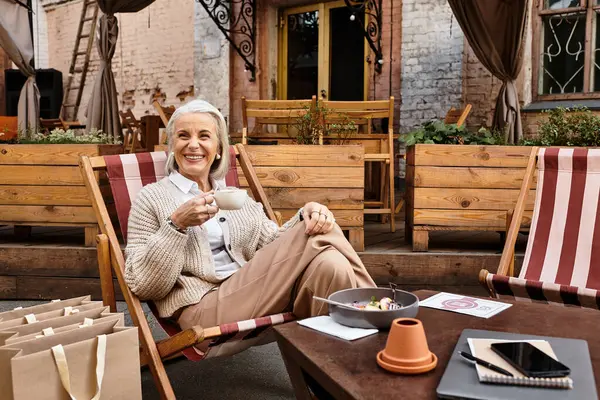 Entspannt in einem charmanten Café genießt eine reife Frau ihren Kaffee mit einem warmen Lächeln draußen. — Stockfoto