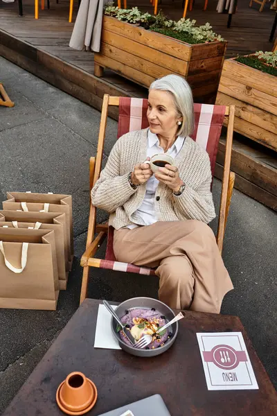 Una donna matura con i capelli grigi si rilassa in un caffè alla moda, sorseggiando caffè e assaporando la vita. — Foto stock