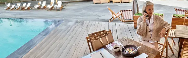 A beautiful woman with gray hair converses on the phone while savoring her meal by the water. — Stock Photo