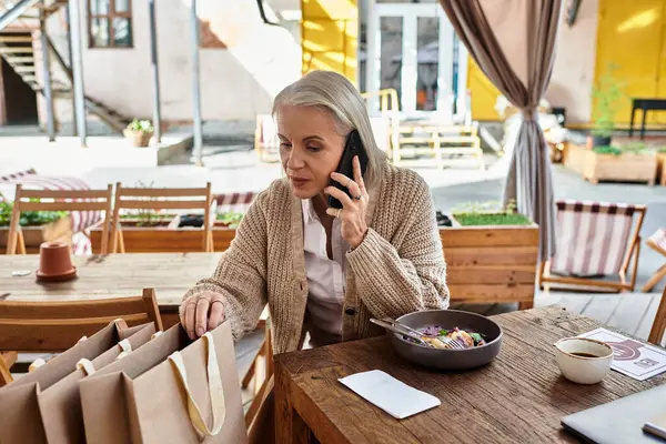 A beautiful mature woman with gray hair engages in a phone conversation while enjoying her meal. — Stock Photo