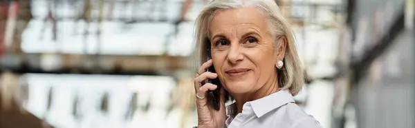 A beautiful mature woman with gray hair speaks on the phone while outdoors near buildings. — Stock Photo