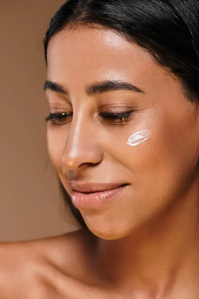 A woman with brunette hair gently applies skincare product on her cheek in a studio setting. — Stock Photo