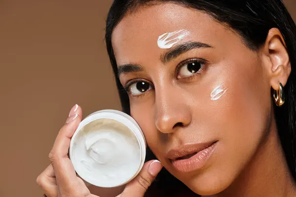 Una donna con i capelli castani mostra la sua routine di cura della pelle in un ambiente da studio. — Foto stock