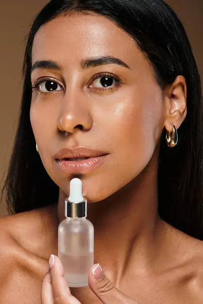 A woman with brunette hair applies skincare serum while showcasing her beauty in a studio setting. — Stock Photo