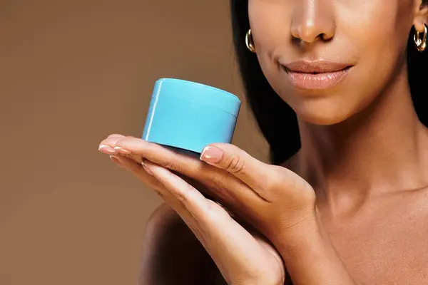 A woman with brunette hair highlights beauty diversity while holding skincare product in studio. — Stock Photo