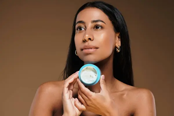 African American woman with brunette hair presents skincare product in studio setting. — Stock Photo