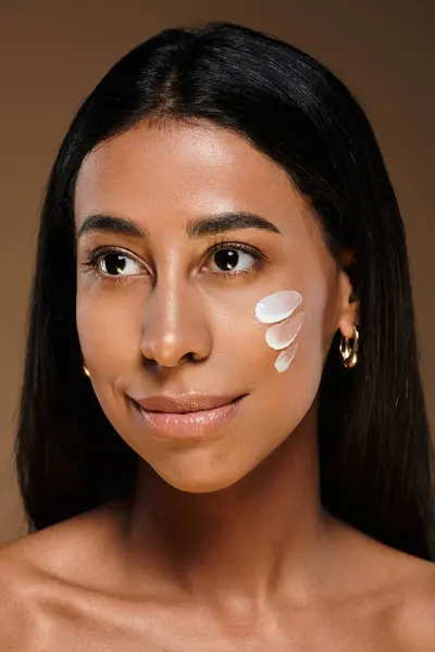 A beautiful African American woman with brunette hair applies skincare product in studio setting. — Stock Photo