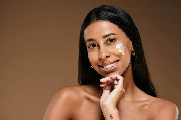 Mujer afroamericana con cabello moreno practica cuidado de la piel mientras sonríe en un estudio. - foto de stock