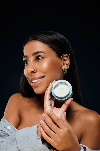 A confident woman holds a body care product while demonstrating skincare in a studio setting. — Stock Photo