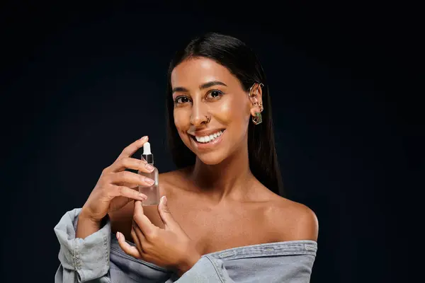 Confident woman demonstrates body care products in a dark studio setting with a joyful smile. — Stock Photo