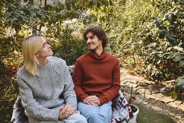 Two handsome young men share a moment of laughter and connection while sitting together in a lush garden. They are dressed in cozy sweaters, enjoying the tranquil atmosphere and each others company. — Stock Photo