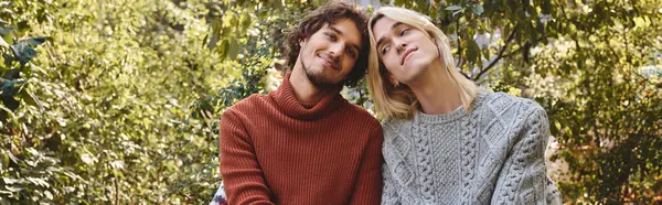 Jovem casal gay amoroso compartilhar um momento alegre em um jardim vibrante. Vestidos com camisolas aconchegantes, eles se inclinam para perto, enquanto cercados por vegetação, irradiando calor e amor à luz do sol da tarde. — Fotografia de Stock