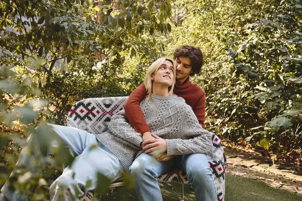 Dans un jardin animé, deux jeunes hommes partagent un moment tendre, embrassant joie et affection. — Photo de stock