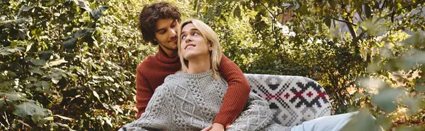 In a serene garden, a handsome young man embraces his partner joyfully. The couple shares a tender moment, wrapped in cozy sweaters, highlighting their love against the vibrant greenery of nature. — Stock Photo