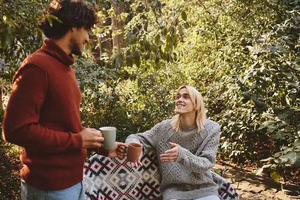 In a serene outdoor setting, two handsome young people share a warm conversation while holding steaming mugs. — Stock Photo