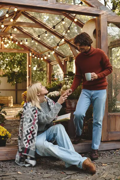 Em um jardim sereno, duas pessoas jovens e bonitas se divertem. Um oferece uma bebida quente, acrescentando à atmosfera amigável de alegria e conexão no paraíso ao ar livre. — Fotografia de Stock