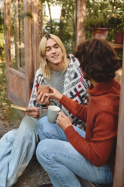 Engaging in warm conversation, two young men share a delightful moment over cups of coffee. Wrapped in a soft blanket, they enjoy a picturesque afternoon surrounded by natures beauty and tranquility. — Stock Photo