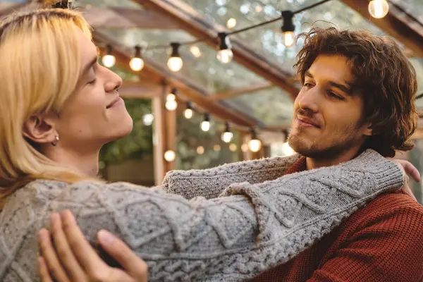 In a charming space filled with twinkling lights, Young loving gay couple share a tender embrace, radiating warmth and affection. The atmosphere is serene, enhancing their emotional connection and joy. — Stock Photo