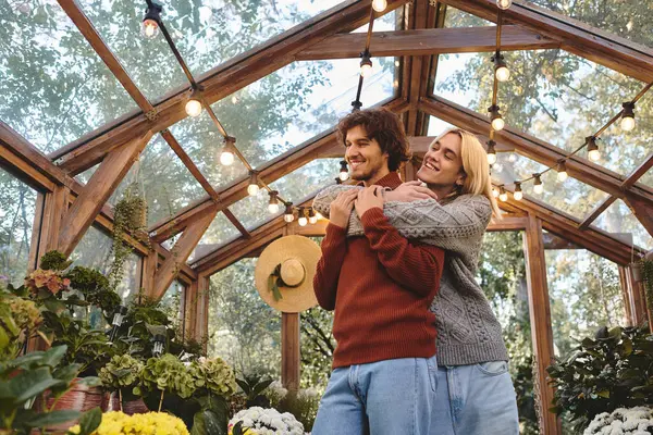 In a charming greenhouse adorned with lush plants and twinkling lights, a young couple shares an affectionate moment. They are surrounded by natures beauty, radiating joy and love. — Stock Photo