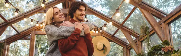 Young loving gay couple share a joyful embrace inside a charming greenhouse adorned with greenery. — Stock Photo