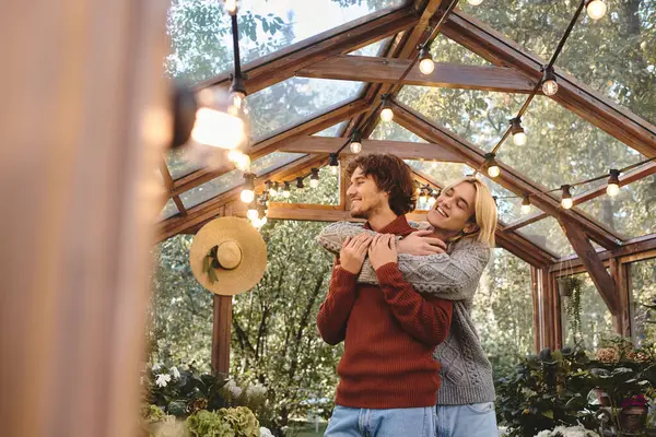 In a vibrant greenhouse filled with greenery, a young couple shares a tender embrace, radiating happiness. Soft sunlight filters through, creating a warm atmosphere as they connect deeply. — Stock Photo
