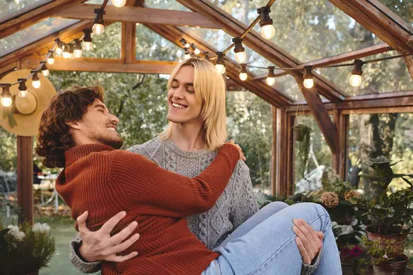 Young loving gay couple are sharing a joyful moment in a beautifully designed greenhouse. With vibrant plants around them, their laughter and affection fill the air, creating a warm atmosphere. — Stock Photo
