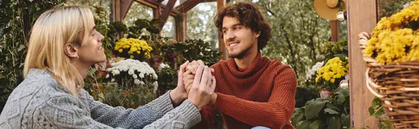 In a lush garden adorned with blooming flowers, a young couple exchanges tender smiles and heartfelt gestures, capturing a moment of joy and connection. The warm setting enhances their vibrant energy. — Stock Photo