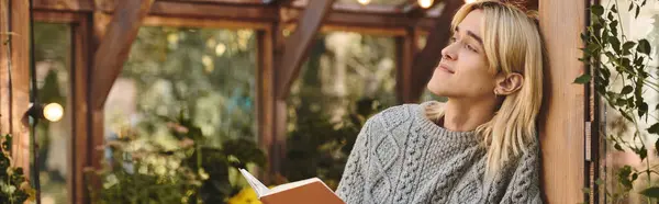 A young, handsome man relaxes in a serene garden setting, enjoying moments of reflection while reading a book. The warm sunlight filters through the greenery, creating a peaceful atmosphere. — Stock Photo