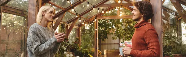 Young loving gay couple engage in a warm conversation inside a vibrant greenhouse illuminated by soft lights. Surrounded by lush greenery, they enjoy each others company and share smiles. — Stock Photo