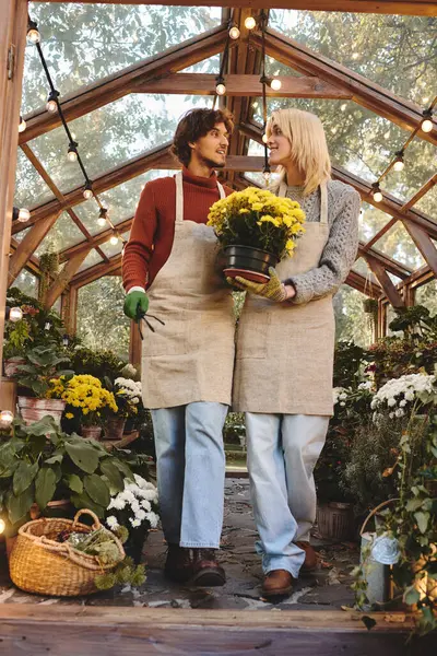 Two young, fashionable men enjoy their time in a colorful greenhouse, nurturing beautiful flowers. — Stock Photo
