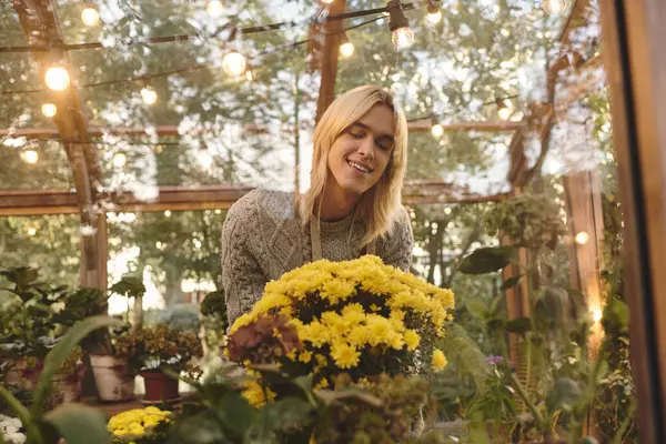 Las flores brillantes llenan el aire de esperanza mientras un joven sonríe suavemente mientras atiende a un ramo. Rodeado de vegetación, encuentra alegría en la belleza de la naturaleza durante una tarde tranquila. - foto de stock
