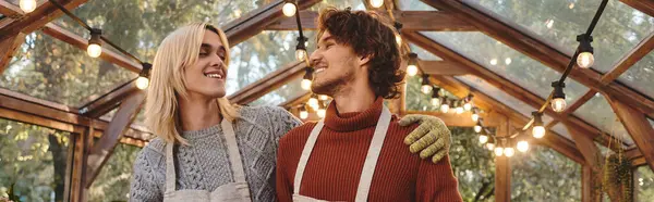 In a beautifully decorated greenhouse filled with warm lights, a young couple shares laughter and affection. — Stock Photo