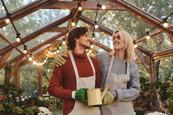 In a charming greenhouse filled with greenery, a young couple stands close, sharing smiles. — Stock Photo
