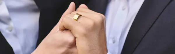 Two young and handsome men clasp hands, showcasing a beautiful golden ring that symbolizes their deep bond. Surrounded by warm sunlight, they share a tender moment filled with joy. — Stock Photo