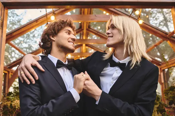 Two handsome young men stand close together in a magical garden atmosphere, their love evident as they share a joyful moment. The charming backdrop of glowing lights adds to the romantic ambiance. — Stock Photo