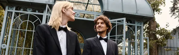 Two young and handsome men dressed in chic tuxedos share a joyful moment together amidst a beautiful outdoor setting. Laughter and happiness fill the air as they stroll gracefully. — Stock Photo