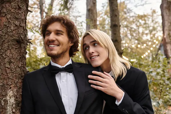 Two young men share a warm embrace in a picturesque forest, surrounded by trees and soft lighting. Their smiles reflect love and joy during a special occasion, creating a serene atmosphere. — Stock Photo