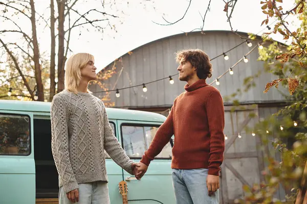 Young loving gay couple share a tender moment, hands intertwined, against a charming vintage van backdrop. Soft lighting and autumn leaves create a warm atmosphere perfect for connection. — Stock Photo