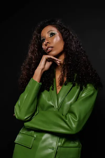 Confident woman showcases her beauty in a chic green ensemble with vibrant makeup in a studio. — Stock Photo