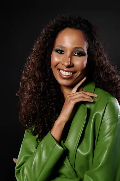 Beautiful woman with curly hair showcases a striking green outfit and a captivating smile. — Stock Photo