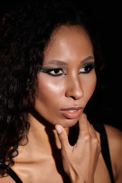 A stunning woman poses confidently, highlighting her makeup and natural beauty against black. — Stock Photo