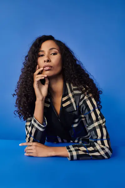 A beautiful woman elegantly poses with stunning curly hair against a vibrant blue backdrop. — Stock Photo