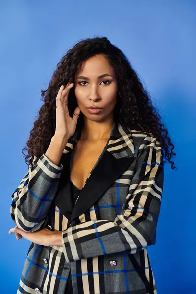 A confident woman showcases her charm and style against a bold blue background. — Stock Photo