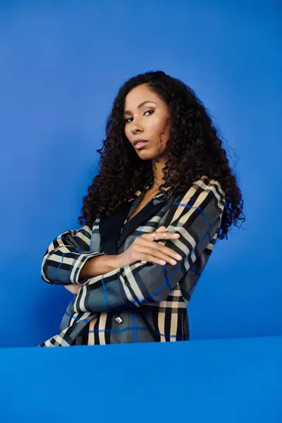 A confident woman showcases her beauty and style while striking a powerful pose against blue. — Stock Photo