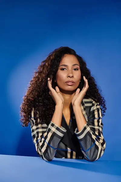 Belle femme aux cheveux bouclés met en valeur son style et sa grâce dans un cadre bleu frappant. — Photo de stock