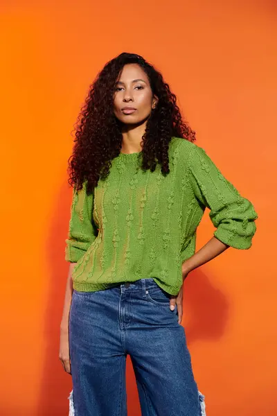 A confident woman poses against a vibrant orange backdrop, flaunting her unique fashion style. — Stock Photo