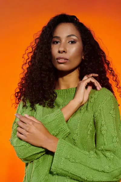 Curly haired woman in a green sweater poses against a glowing orange background. — Stock Photo